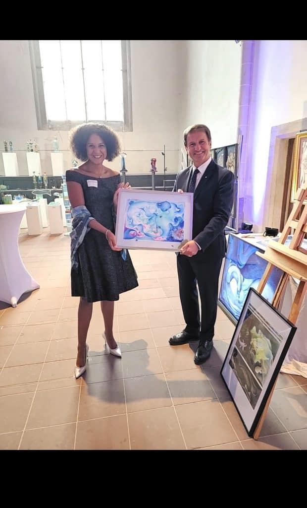 "Auf diesem Foto sind Michaela de Luxe und Landrat Michael Stickeln bei der Vernissage/Eröffnung der Ausstellung zu sehen. Beide halten stolz ein von Michaela gemaltes Bild in ihren Händen"