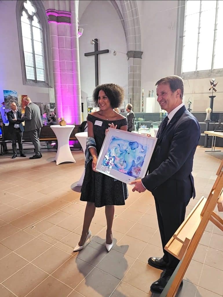 "Auf diesem Foto sind Michaela de Luxe und Landrat Michael Stickeln bei der Vernissage/Eröffnung der Ausstellung zu sehen. Beide halten stolz ein von Michaela gemaltes Bild in ihren Händen"